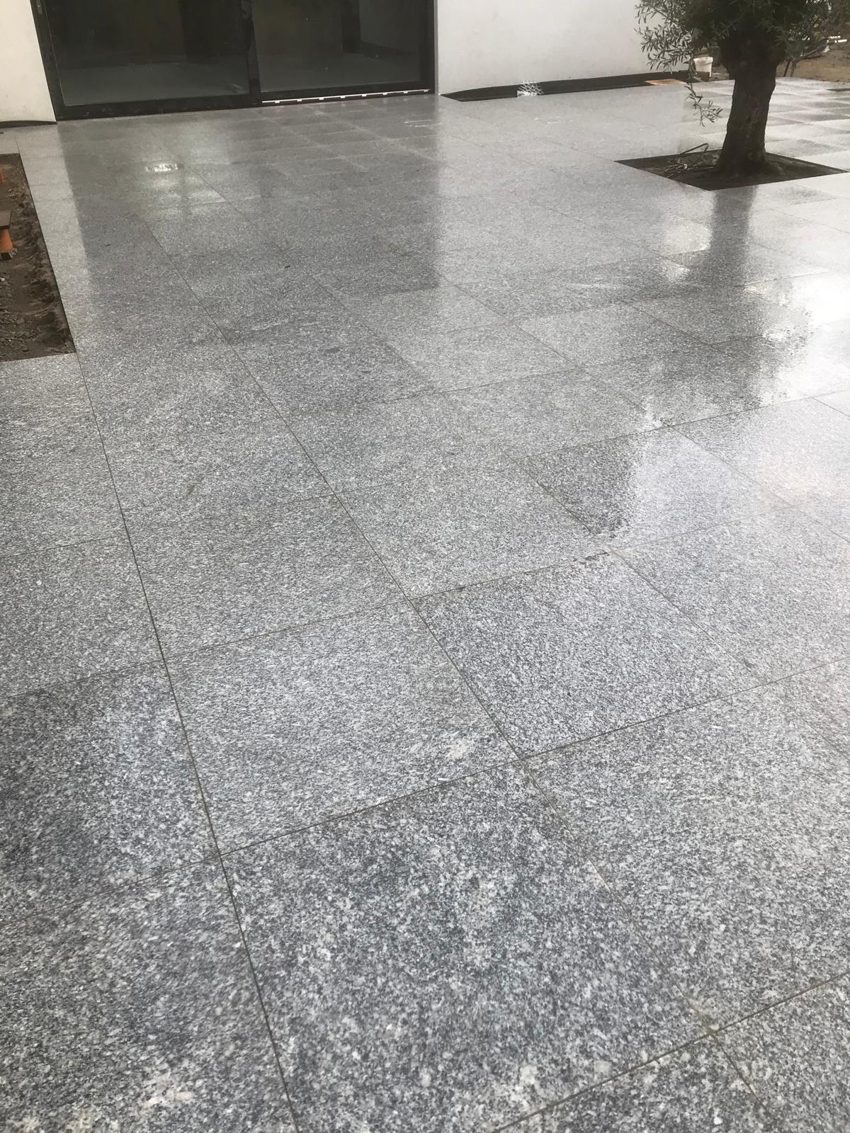 Close view of a wet light granite slab patio showing tight, even joints running up to full height glazing