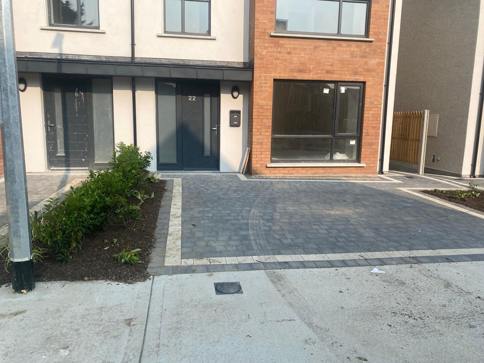 Charcoal block paved driveway with a pale border course and a subtle circular pattern set into the paving, in front of new brick and rendered houses