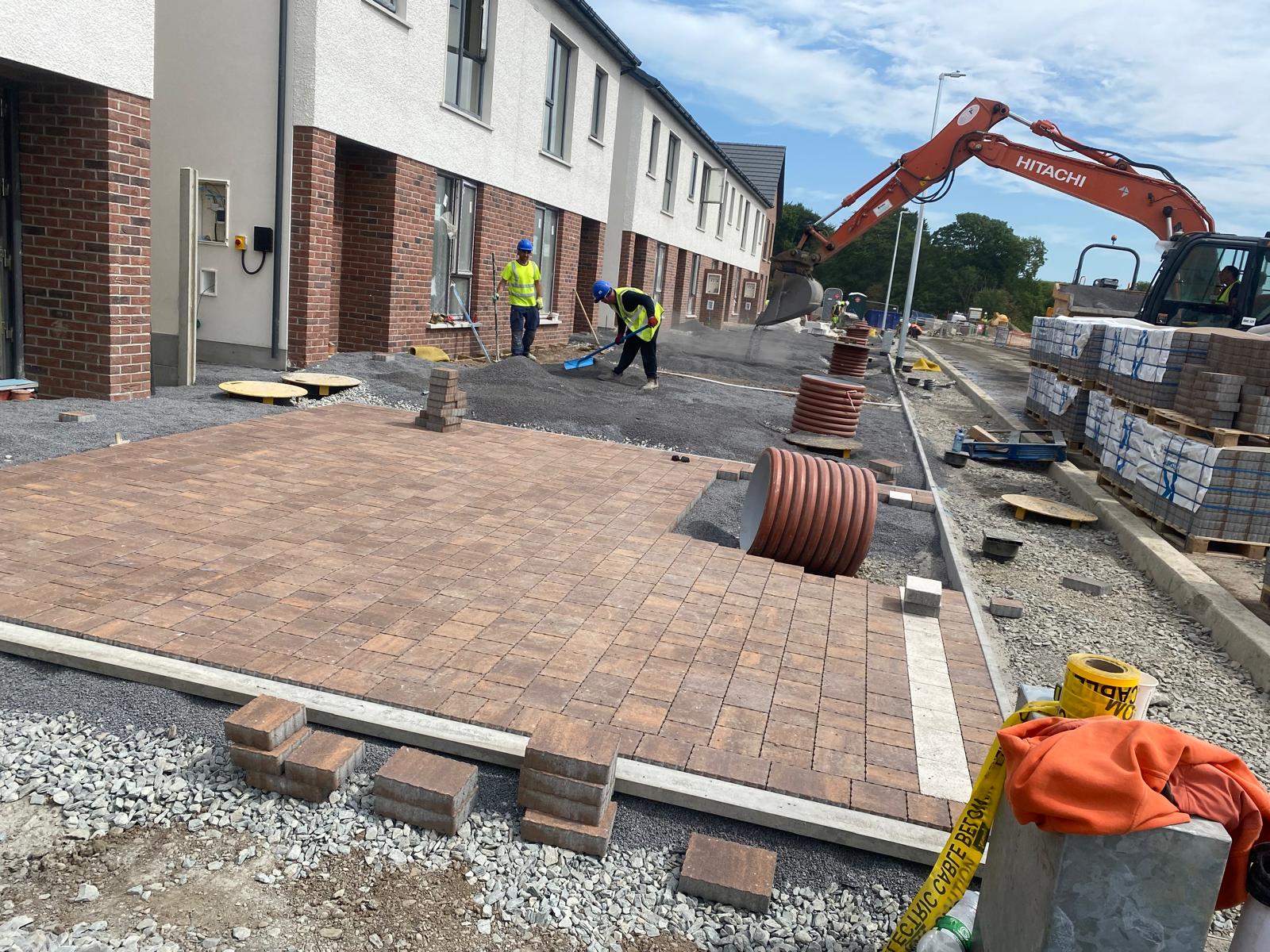 Brindle block paving being laid in a large bay with concrete edge restraints while the team prepares the adjoining stone base and drainage on a housing site