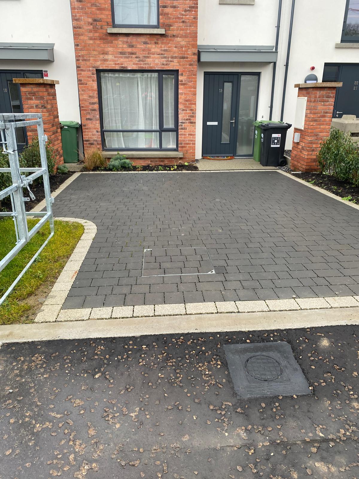 Dark grey block paved driveway with a wide pale border course and curved corner, running up to the front doors of a brick and rendered terrace