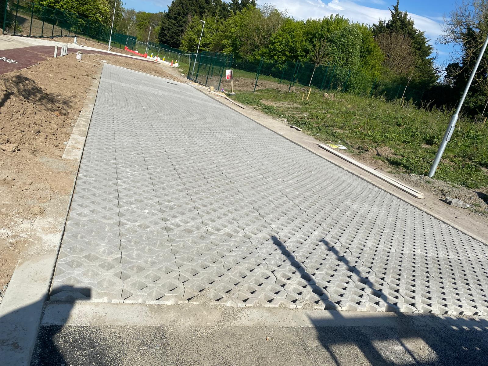 Wide access route laid in open cell concrete grid paving on a prepared base, edged with concrete kerbs alongside fresh ground and fencing