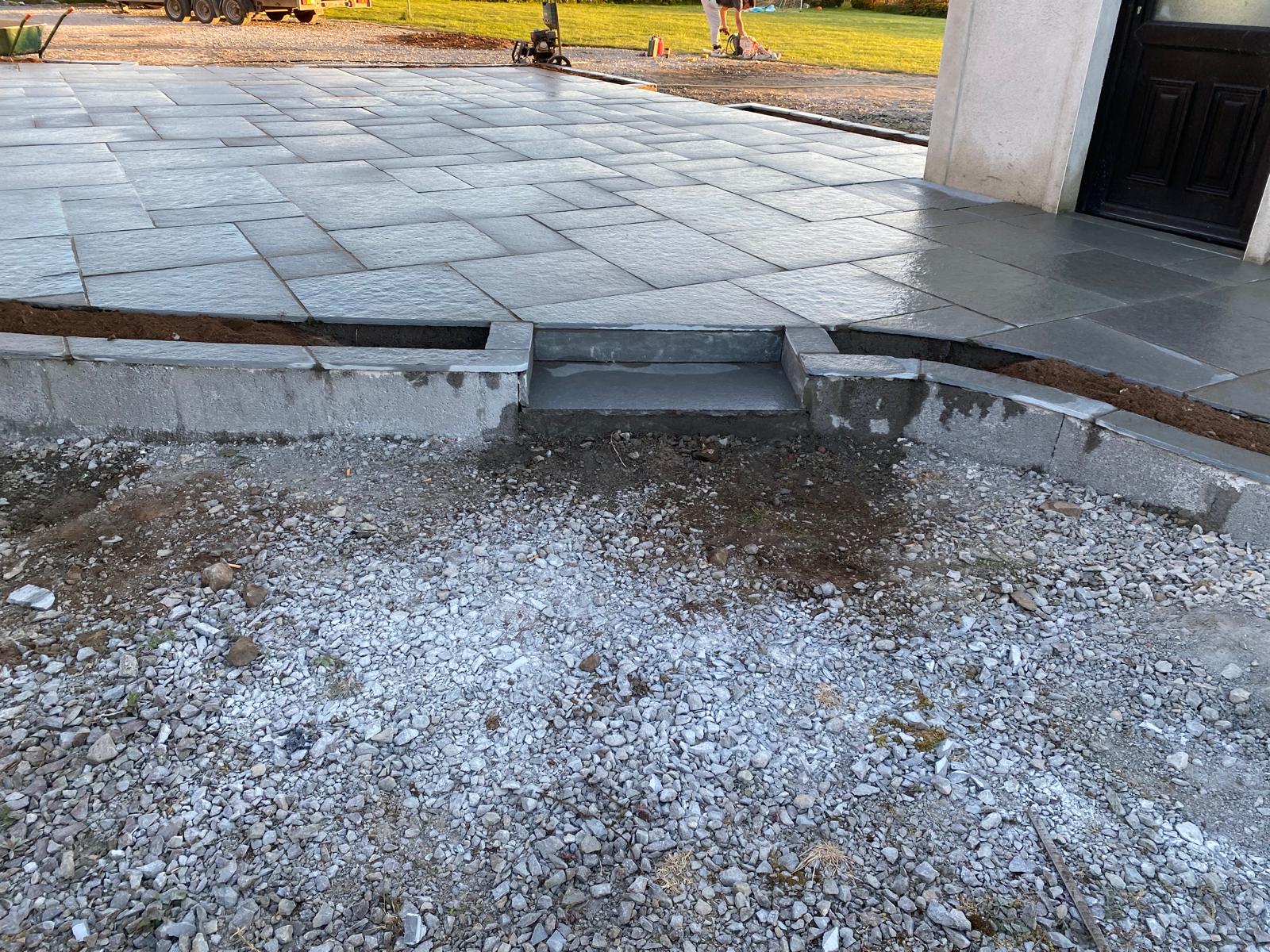 Raised sandstone patio with a block built edge, capped border and a single wide step down to a stone base area beside a house entrance