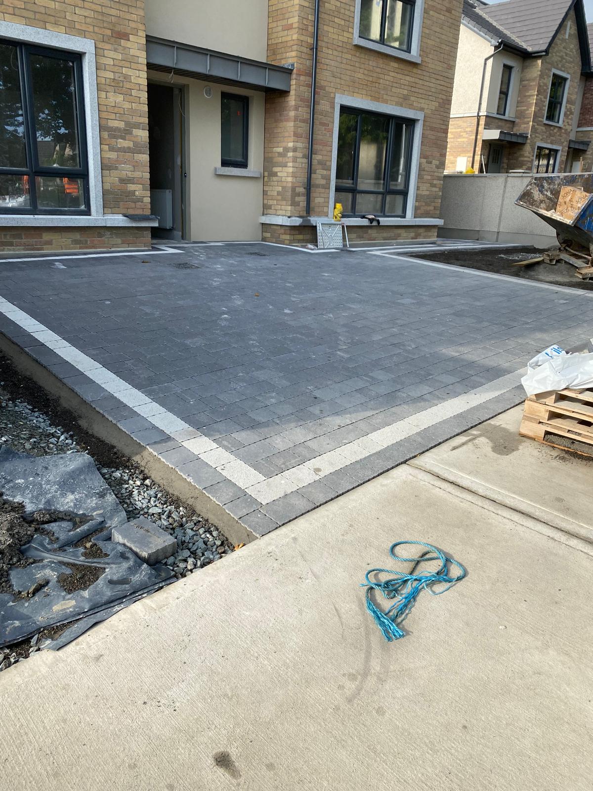 Charcoal block paved parking area with a light granite border course and stepped edge detail in front of new brick and rendered houses
