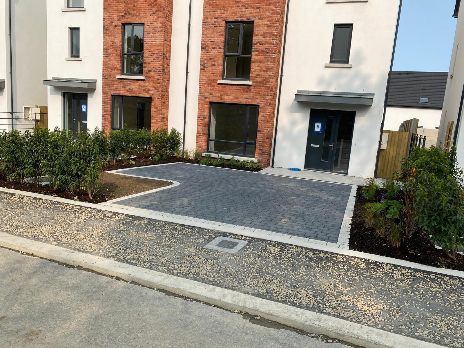 Charcoal block paved driveway with a pale border course serving two new houses, edged by fresh planting beds and gravel