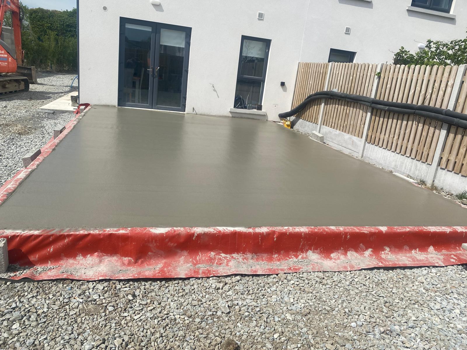 Freshly poured and floated concrete base with formed edges and protective membrane, laid outside patio doors on a compacted stone sub base