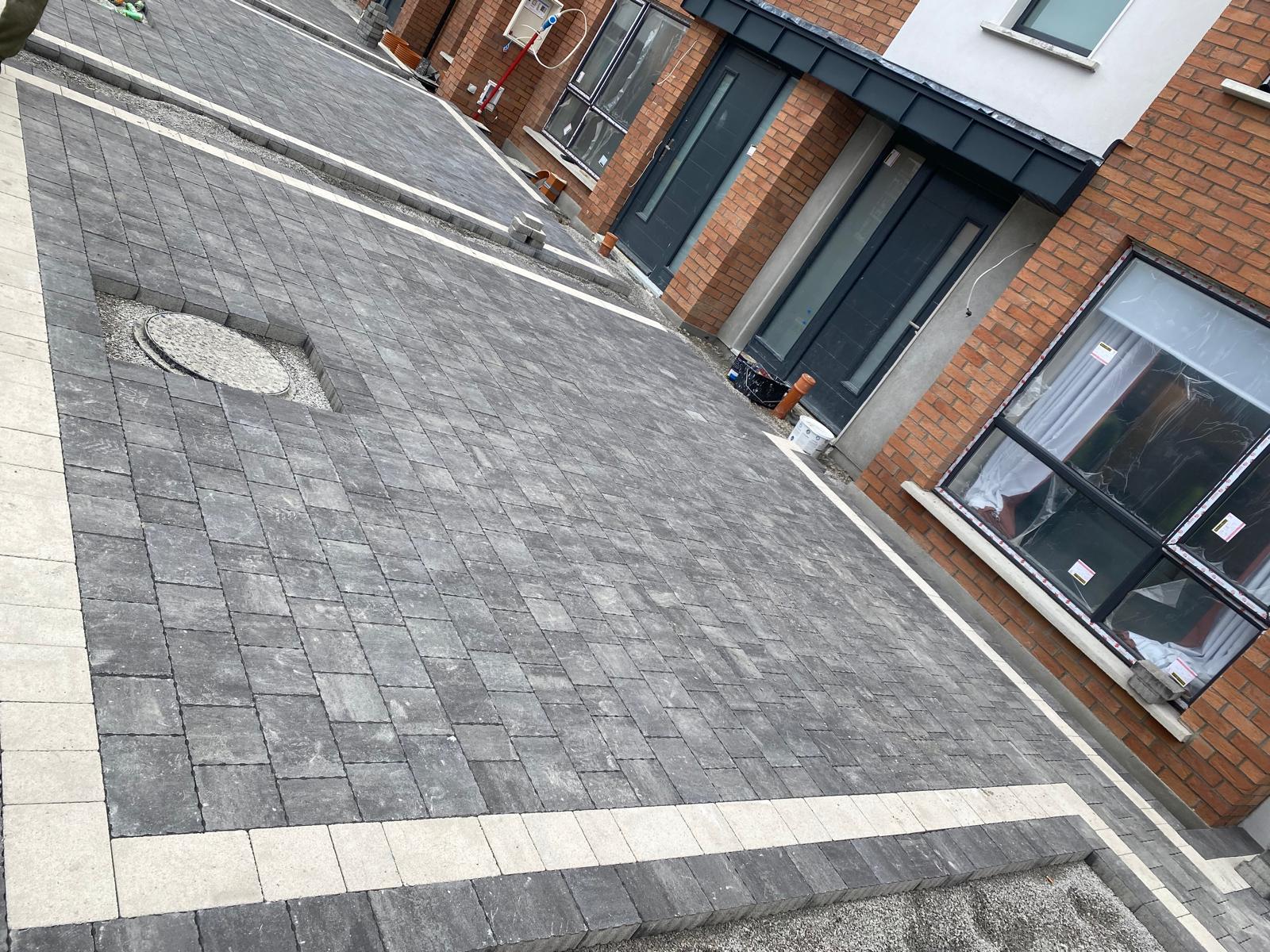 Large charcoal block paved courtyard with contrasting pale border courses running alongside brick townhouses